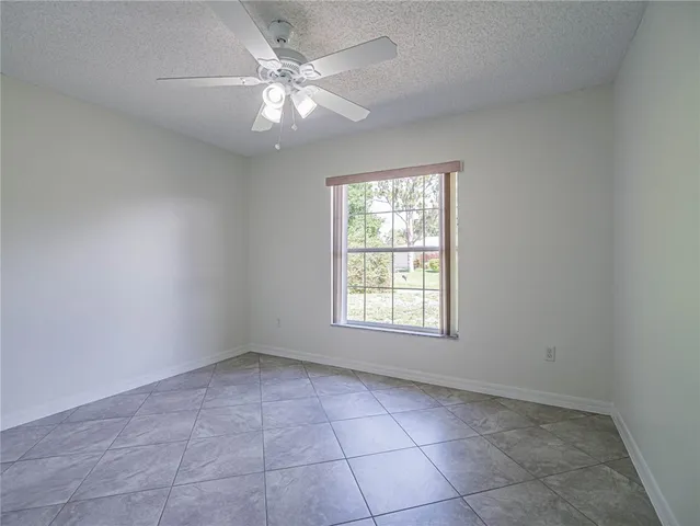 an empty room with chandelier fan and windows
