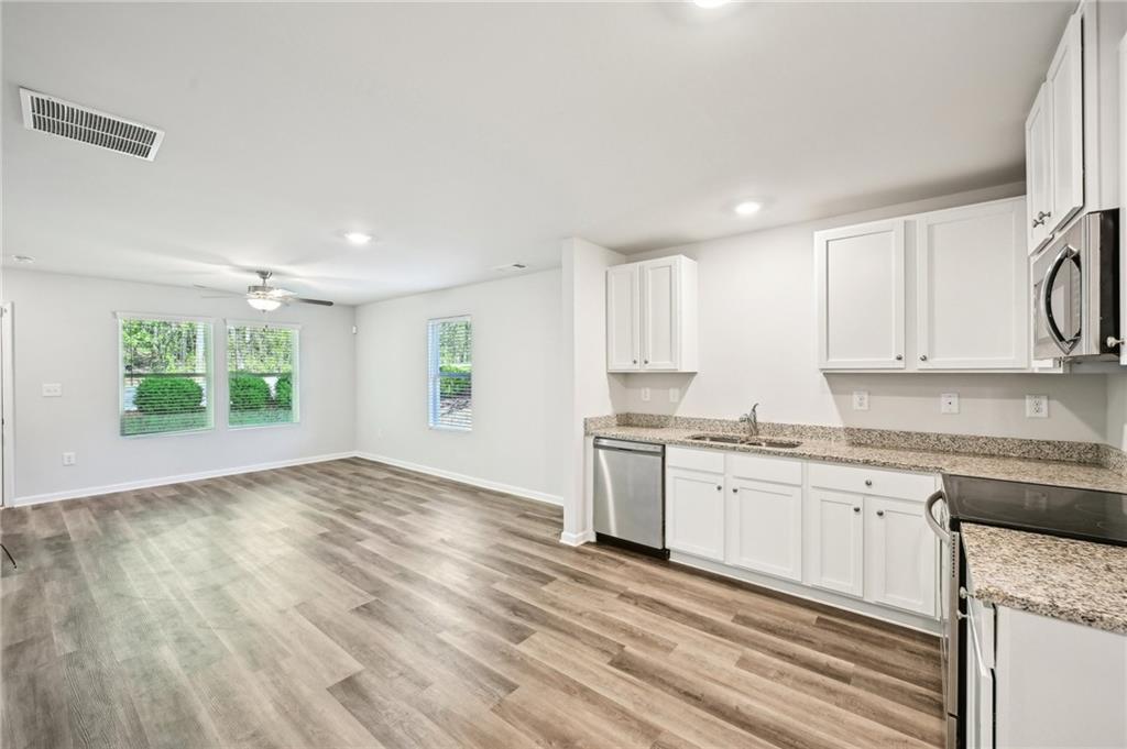 4437 Ben Hill Road Atlanta, GA 30349 - Photo 9 of 40 a kitchen with granite countertop a stove a sink and white cabinets with wooden floor