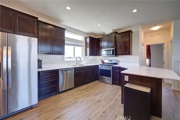 a kitchen with stainless steel appliances kitchen island granite countertop wooden cabinets a refrigerator a sink a stove a microwave and wooden floors