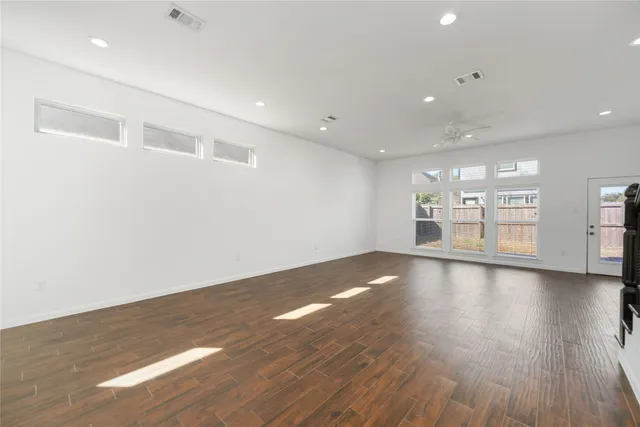 a view of empty room with wooden floor and kitchen