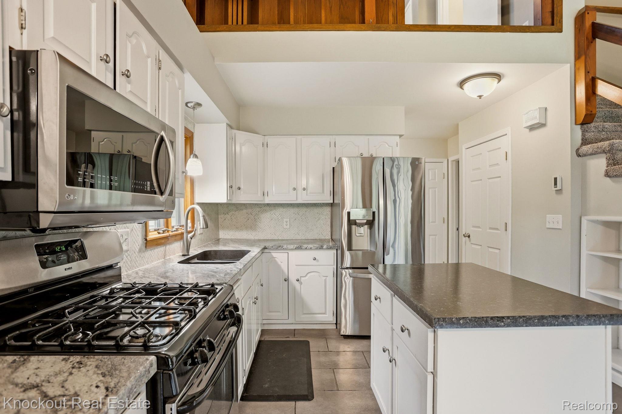 1608 South Pinnebog Road Bad Axe, MI 48413 - Photo 18 of 54 Kitchen featuring stainless steel appliances, a center island, white cabinetry, backsplash, and light tile patterned floors