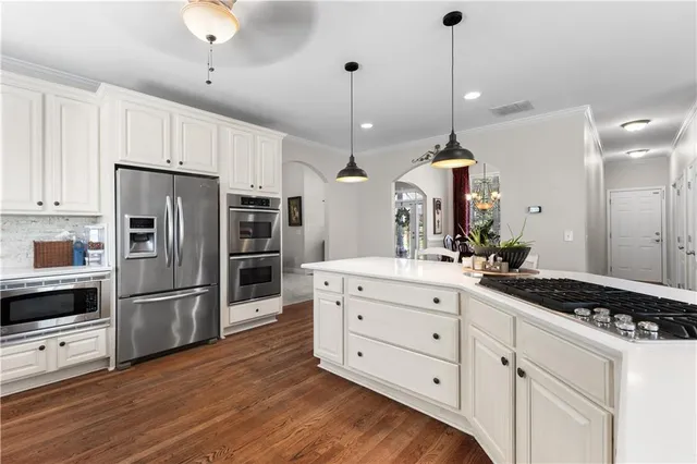 a kitchen with stainless steel appliances kitchen island a refrigerator a stove and white cabinets with wooden floors