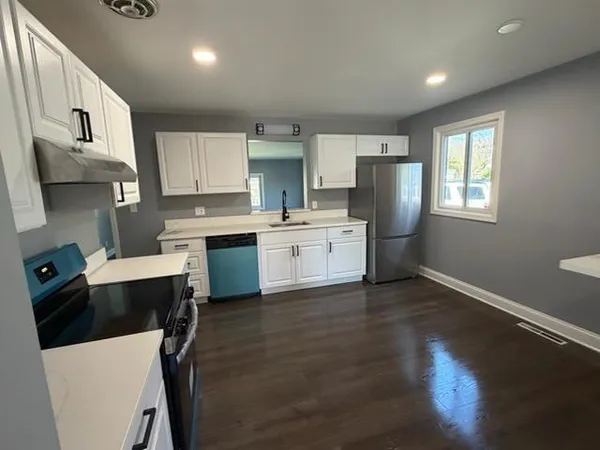 a kitchen with a refrigerator a stove top oven a sink dishwasher and white cabinets with wooden floor