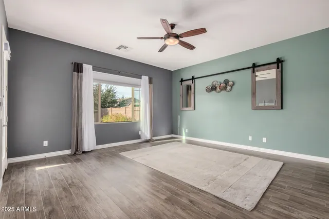 an empty room with wooden floor chandelier fan and windows