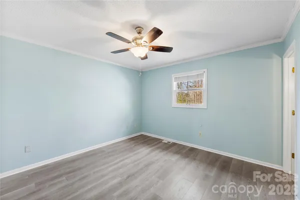 a view of an empty room with wooden floor and a ceiling fan