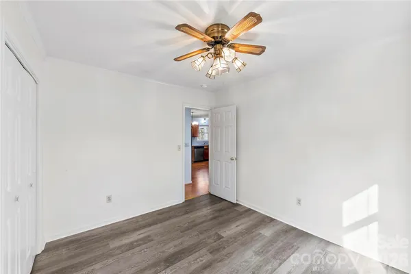 an empty room with a chandelier fan and wooden floor