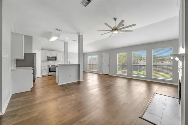 a view of an empty room with wooden floor and a kitchen