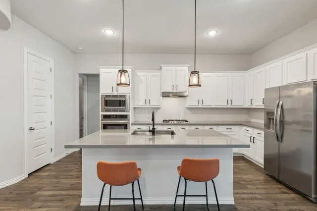 a kitchen with stainless steel appliances granite countertop a sink a stove a refrigerator and island with wooden floor