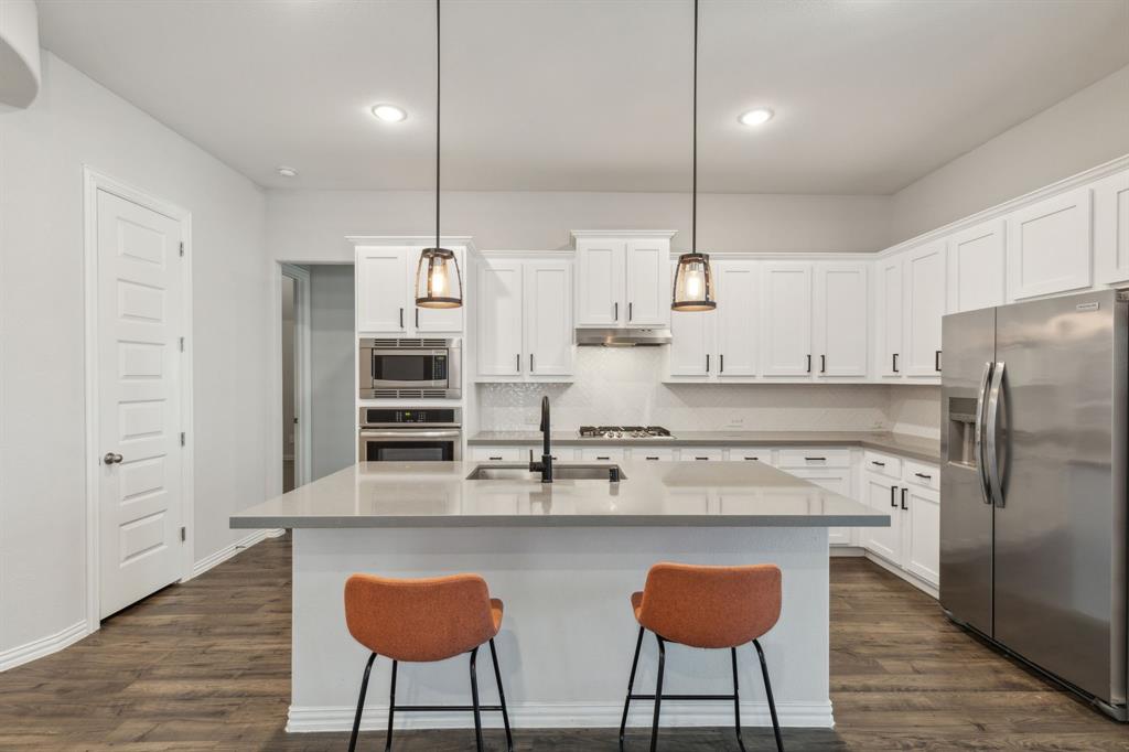 1918 Holy Unity Lane Wylie, TX 75098 - Photo 3 of 19 a kitchen with stainless steel appliances granite countertop a sink a stove a refrigerator and island with wooden floor