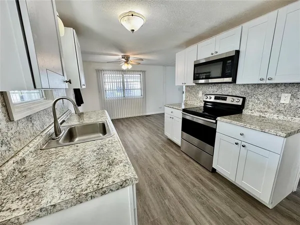 a kitchen with stainless steel appliances granite countertop a sink dishwasher stove and microwave with wooden floor