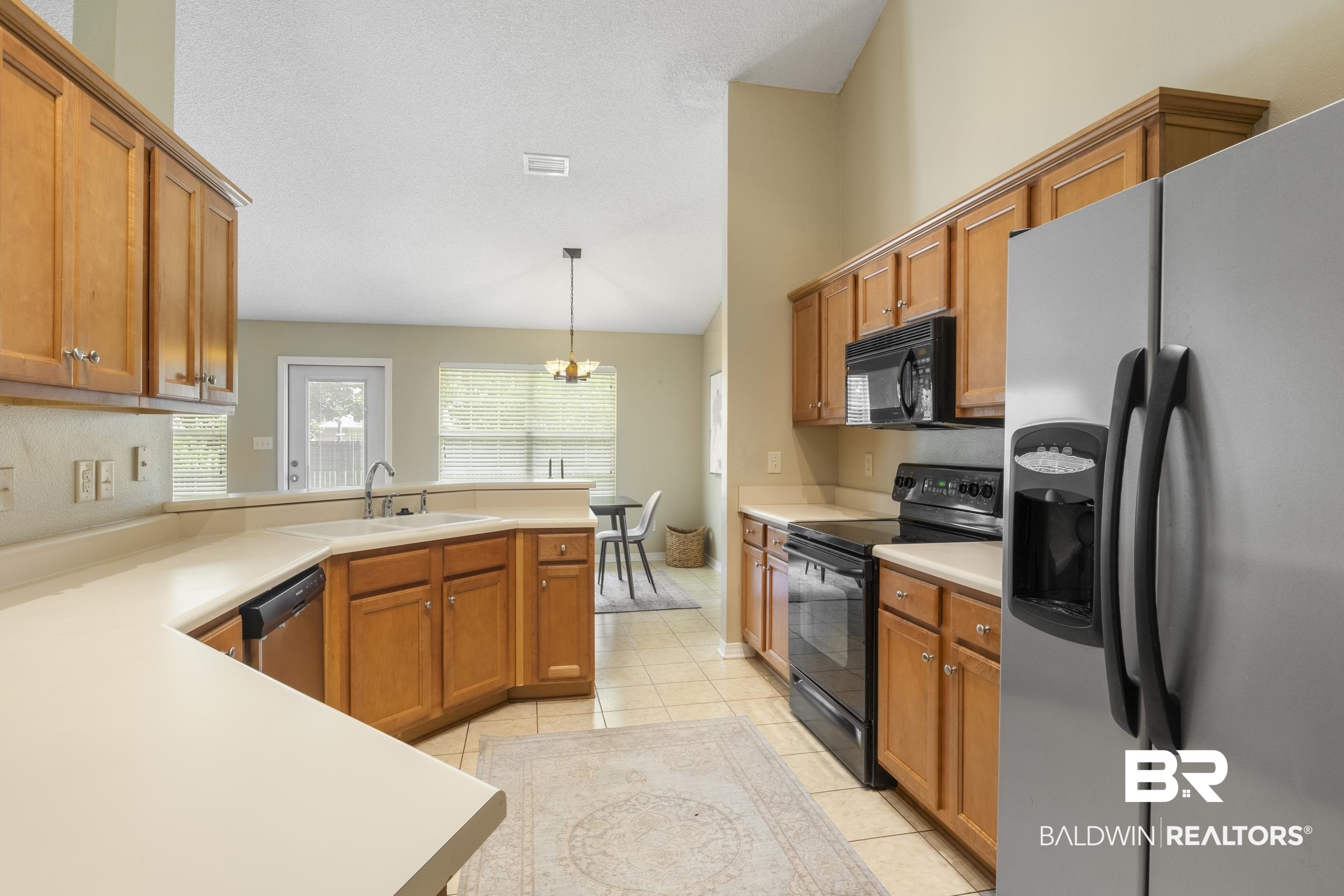 9610 Watkins Drive Fairhope, AL 36532 - Photo 5 of 26 Kitchen featuring light tile patterned flooring, black appliances, decorative light fixtures, sink, and an inviting chandelier