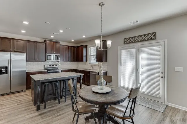 a kitchen with stainless steel appliances kitchen island granite countertop a dining table chairs sink and microwave
