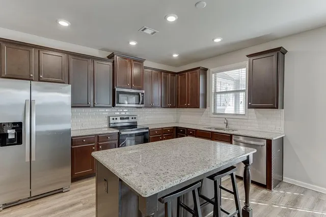 a kitchen with stainless steel appliances granite countertop a kitchen island a stove a refrigerator a sink a dining table and chairs