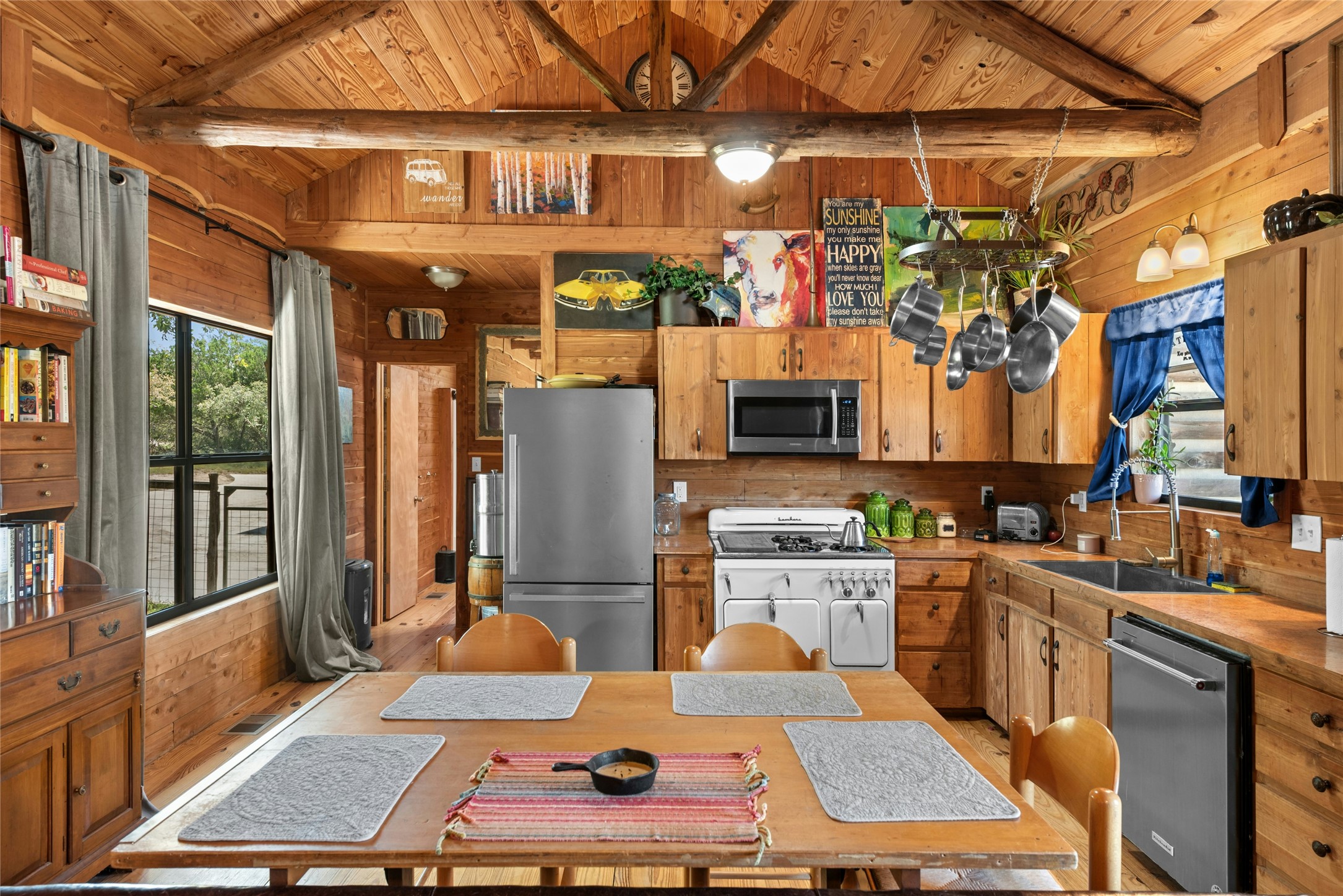 496 Middleton Road Spicewood, TX 78669 - Photo 12 of 40 Open-concept kitchen and dining area featuring natural wood paneling throughout, exposed wood ceiling beams, and a full suite of stainless steel appliances