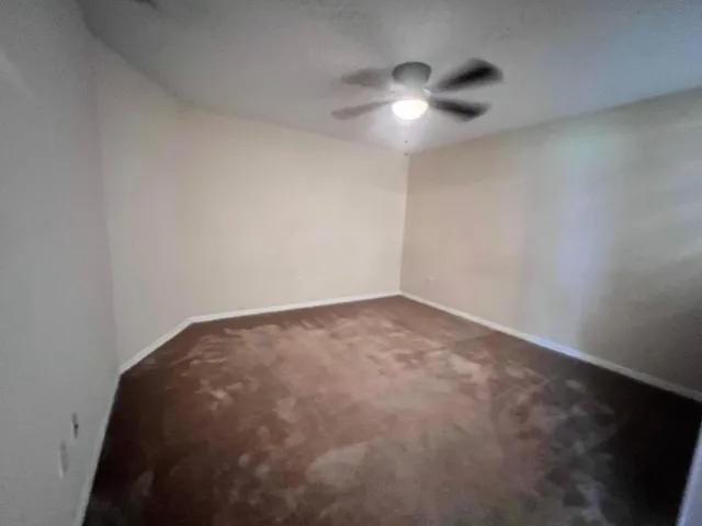 an empty room with chandelier fan and windows