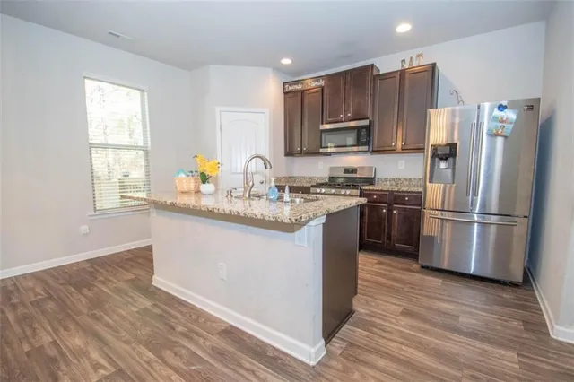 a kitchen with stainless steel appliances granite countertop a sink a stove a refrigerator cabinets and a wooden floor