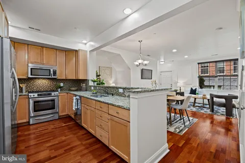 a kitchen with stainless steel appliances granite countertop a refrigerator a stove top oven a sink dishwasher and white cabinets with wooden floor
