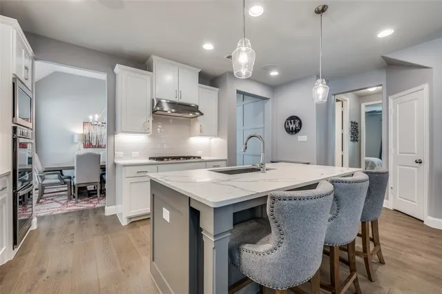 a kitchen with stainless steel appliances granite countertop a stove a refrigerator a kitchen island a dining table and chairs with wooden floor