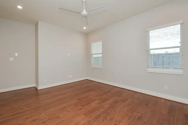 an empty room with wooden floor chandelier fan and windows