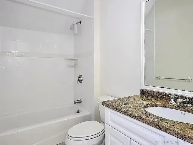 a bathroom with a granite countertop bathtub shower sink vanity and toilet