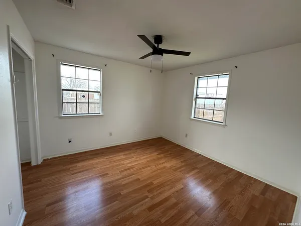 an empty room with wooden floor windows and ceiling fan