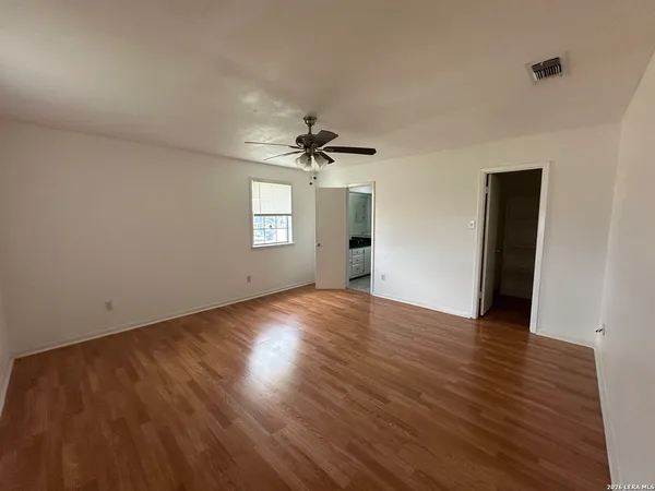 an empty room with wooden floor chandelier fan and windows