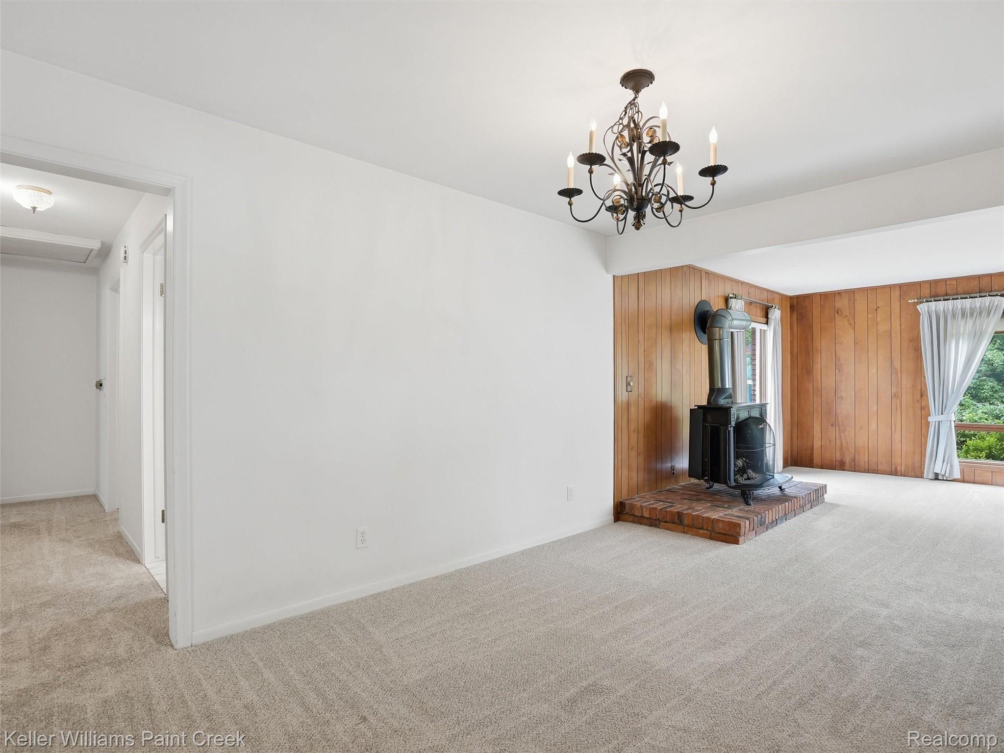 436 Broadleaf Drive Rochester, MI 48306 - Photo 14 of 41 Unfurnished living room with light colored carpet, wood walls, a wood stove, and a chandelier