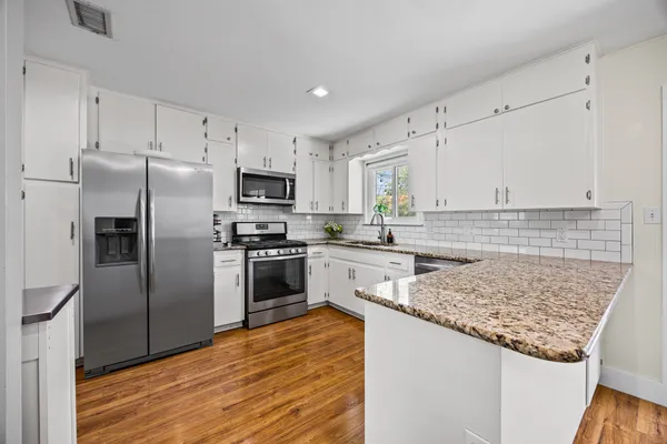 a kitchen with granite countertop a refrigerator oven a sink and white cabinets