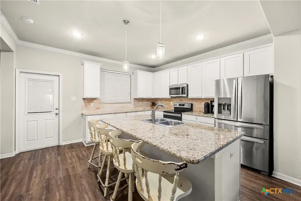 a kitchen with granite countertop stainless steel appliances a refrigerator a stove a sink a center island a dining table and chairs