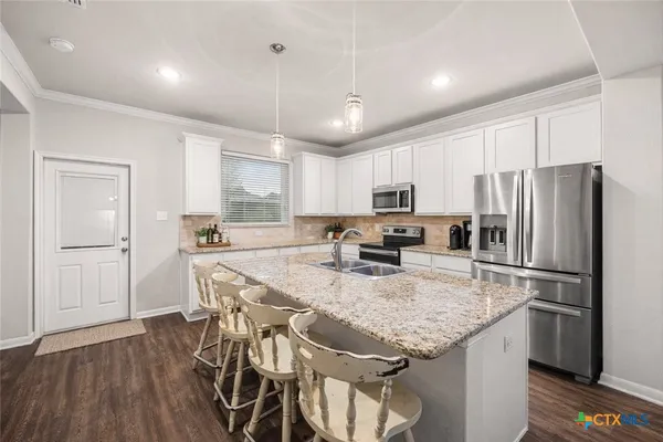 a kitchen with granite countertop stainless steel appliances a refrigerator a stove a sink a center island a dining table and chairs