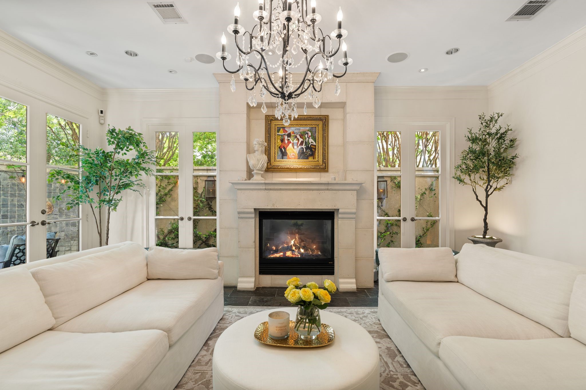 30 Hackberry Lane, Unit A Houston, TX 77027 - Photo 12 of 42 The family room is anchored by a gaslog fireplace with cast-stone mantel set into a dramatic floor-to-ceiling stone surround. Three sets of three-lite double doors—two fixed and one fully functional. A striking multi-tiered chandelier adorned with hanging glass ornaments, complemented by art lighting