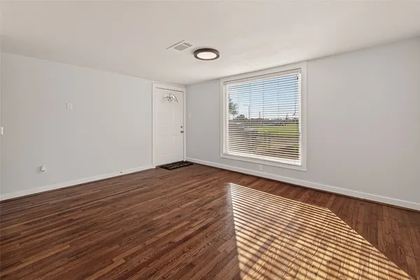a view of an empty room with wooden floor and a window