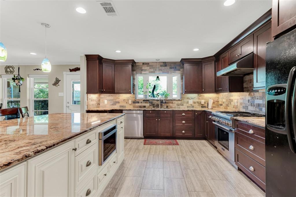 319 East Spring Valley Road Richardson, TX 75081 - Photo 4 of 22 Gourmet kitchen featuring a large island with built-in microwave, wood-finish flooring, recessed lighting, stone backsplash, and dark wood cabinetry