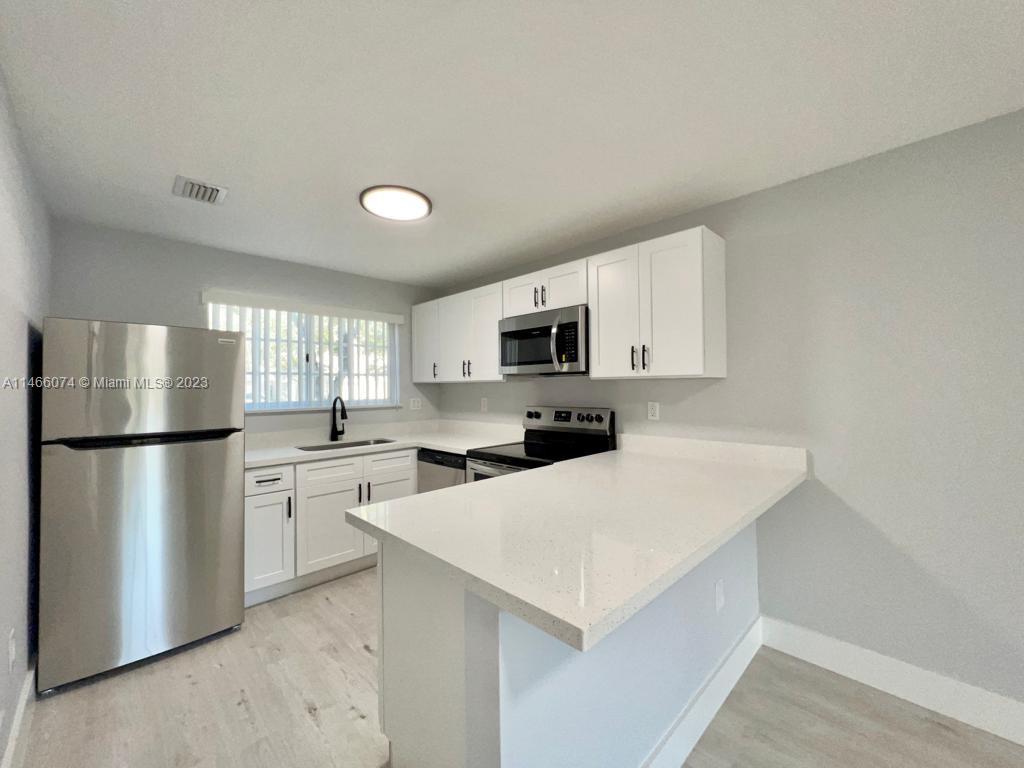 14116 Southwest 260th Street, Unit 106 Homestead, FL 33032 - Photo 7 of 24 a kitchen with a refrigerator a stove top oven a sink and cabinets