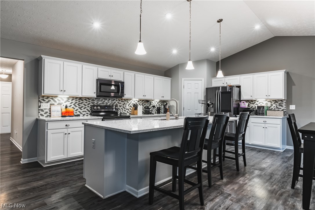 2545 Layman Road Vincent, OH 45784 - Photo 6 of 32 Kitchen featuring backsplash, white cabinets, light countertops, appliances with stainless steel finishes, a center island with sink, a center island, lofted ceiling, dark hardwood flooring, and pendant lighting