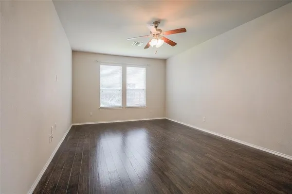 an empty room with wooden floor chandelier fan and windows
