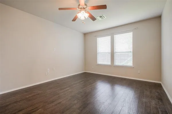 an empty room with wooden floor chandelier fan and windows