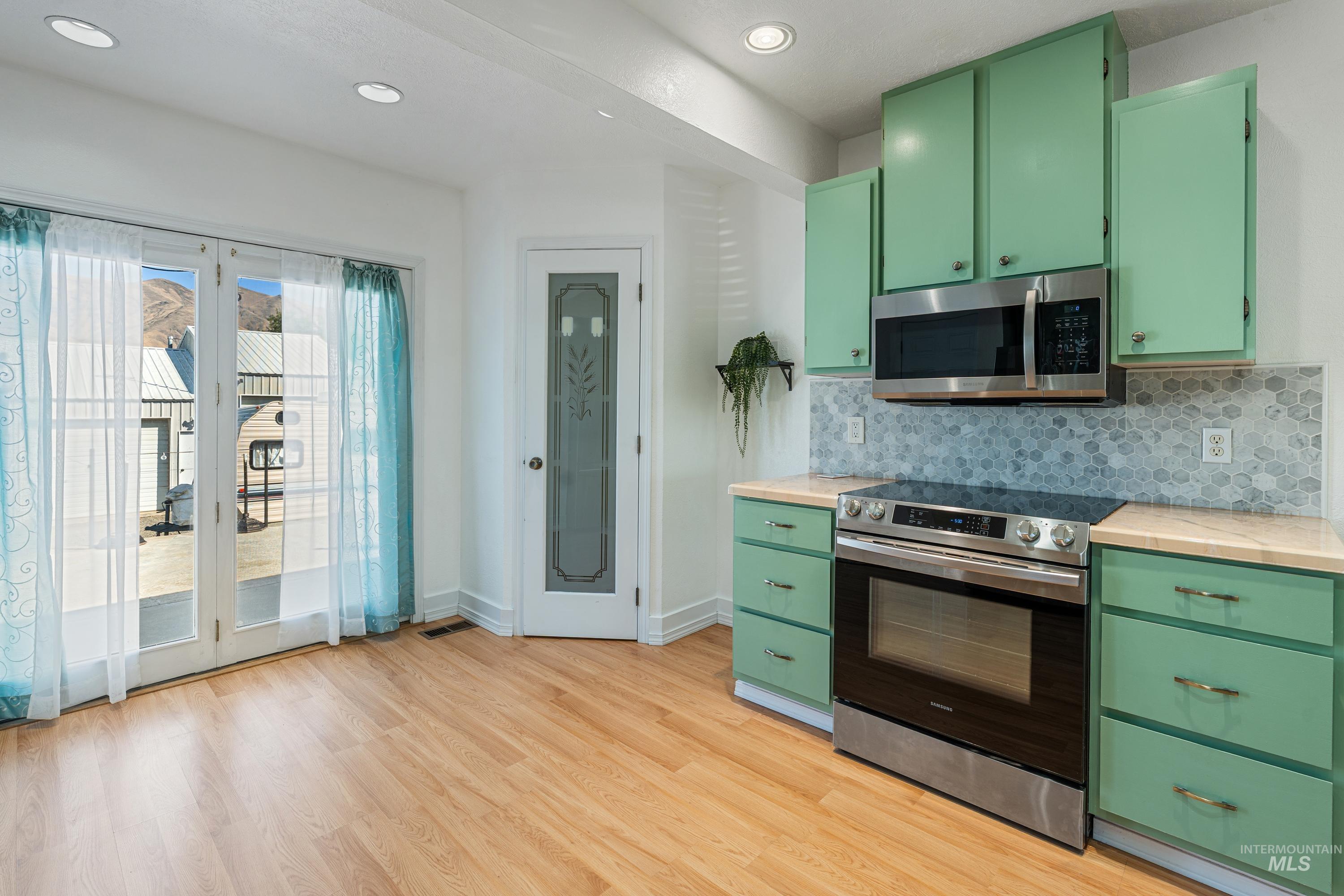1266 Maple Street Clarkston, WA 99403 - Photo 8 of 44 Kitchen with light green cabinetry, stainless steel oven/range, built-in microwave, and wood-finish flooring