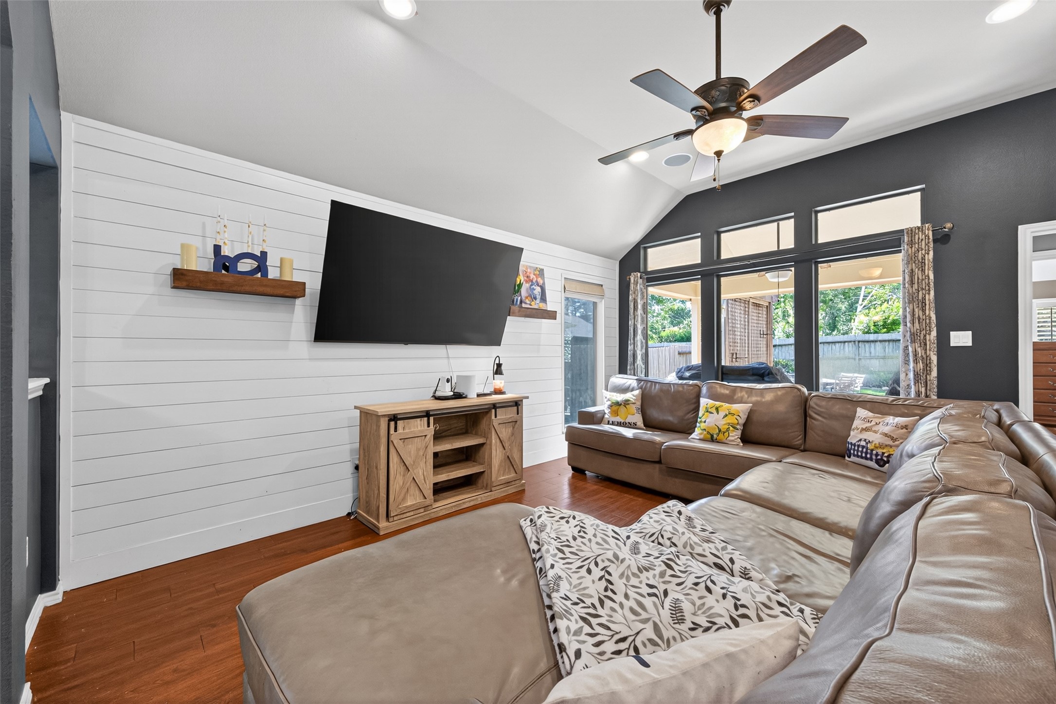 27443 Rebecca Field Lane Spring, TX 77386 - Photo 13 of 31 Spacious living room with vaulted ceilings, featuring shiplap wall, modern ceiling fan. Natural light pours in through large windows overlooking the backyard, enhancing the cozy, open feel.