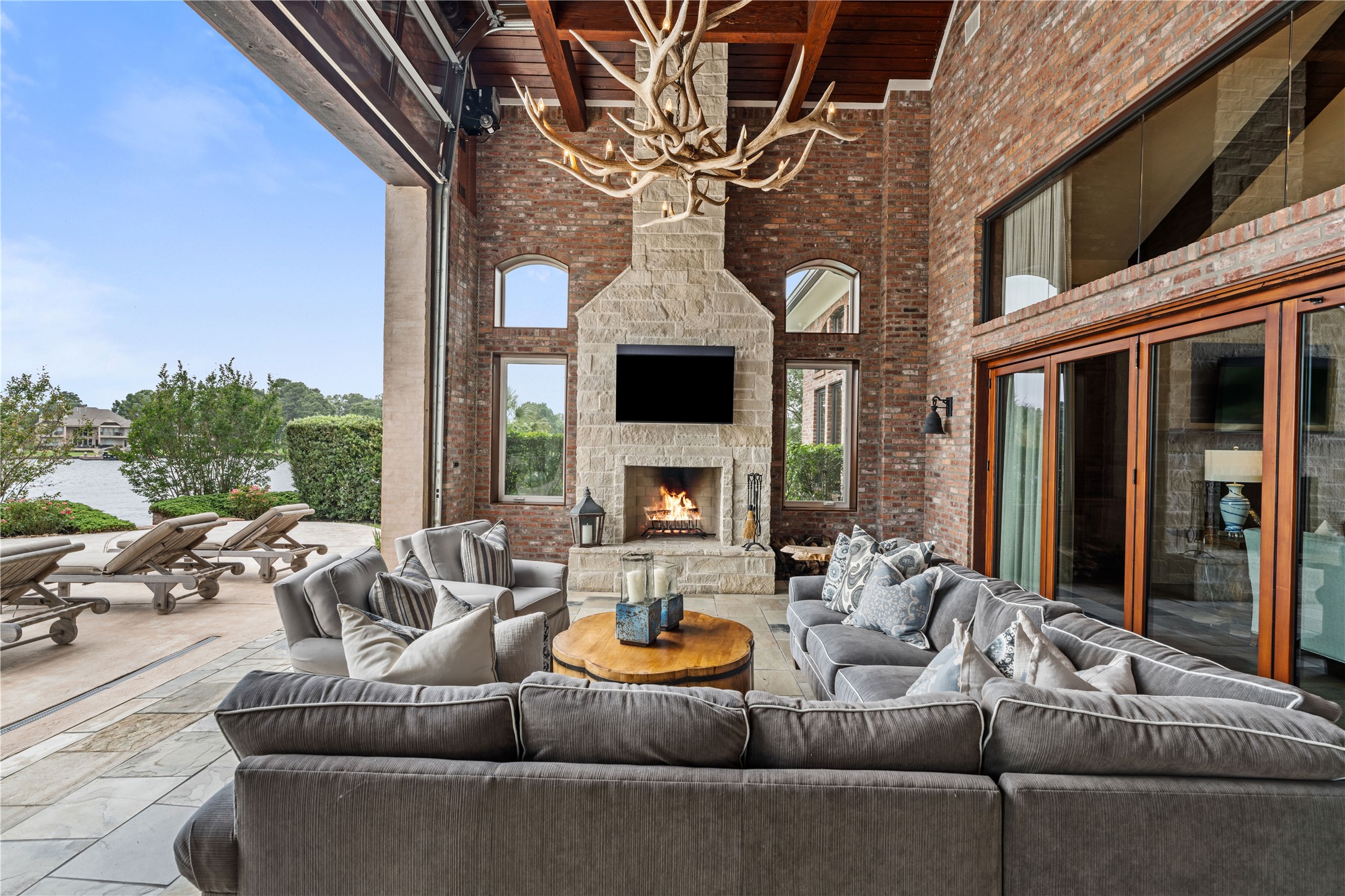 12349 Longmire Trace Conroe, TX 77304 - Photo 34 of 48 Covered lakeside patio with soaring wood ceiling, stone fireplace, and expansive glass doors for seamless indoor-outdoor living.