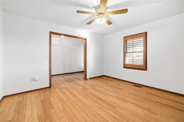 an empty room with wooden floor chandelier fan and windows