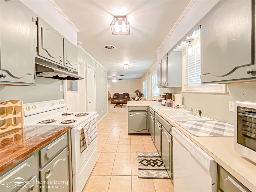 1104 Hickory Street Roscoe, TX 79545 - Photo 12 of 22 Kitchen featuring white appliances, light countertops, light tile patterned flooring, under cabinet range hood, and ornamental molding