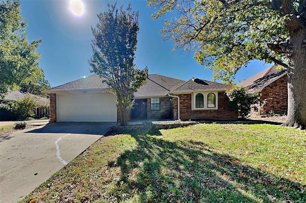 Ranch-style house with concrete driveway, brick siding, a front lawn, an attached garage, and roof with shingles