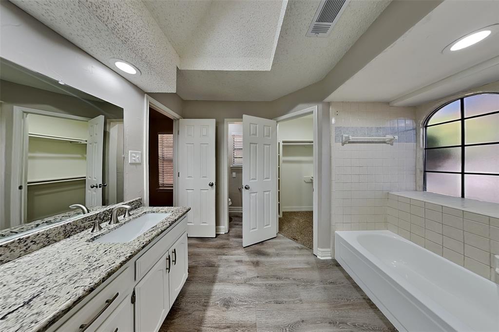 3920 Winston Drive Denton, TX 76210 - Photo 11 of 20 Full bathroom with a spacious closet, vanity, light wood-style flooring, a bath, and a textured ceiling