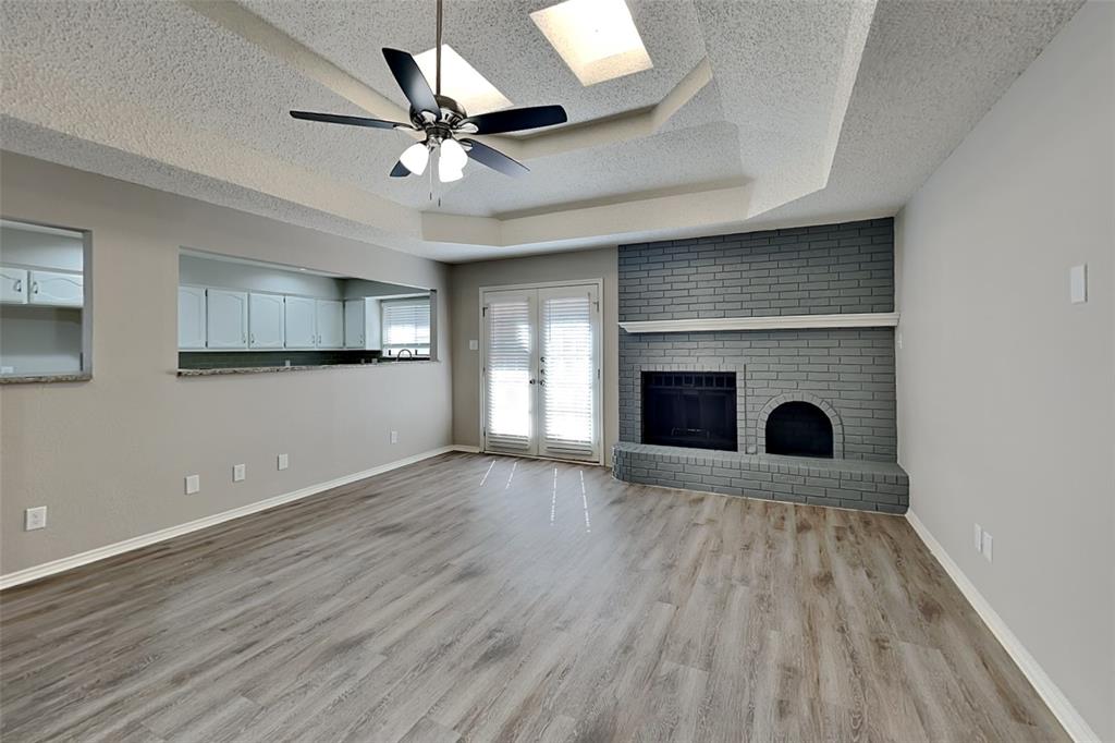 3920 Winston Drive Denton, TX 76210 - Photo 2 of 20 Unfurnished living room featuring a tray ceiling, a ceiling fan, light wood finished floors, a textured ceiling, and a brick fireplace