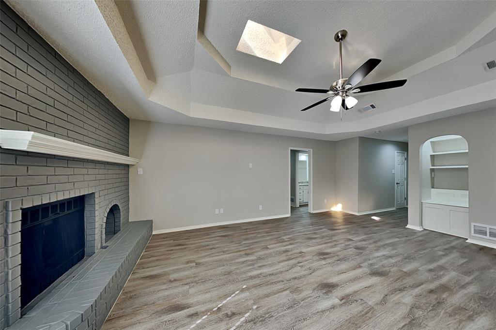 3920 Winston Drive Denton, TX 76210 - Photo 4 of 20 Unfurnished living room with a skylight, a raised ceiling, a fireplace, light wood-style flooring, and a textured ceiling
