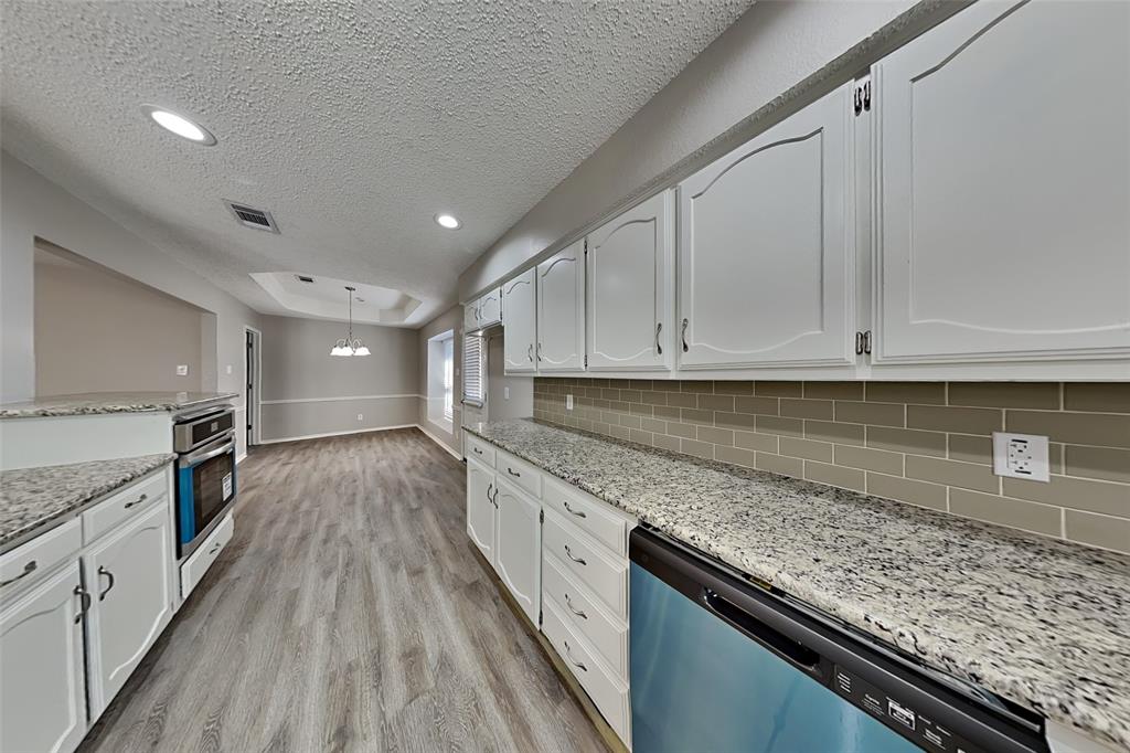 3920 Winston Drive Denton, TX 76210 - Photo 6 of 20 Kitchen featuring a textured ceiling, dishwashing machine, light stone counters, decorative light fixtures, and white cabinets