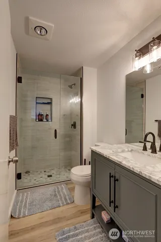 a bathroom with a granite countertop sink a toilet a mirror and shower