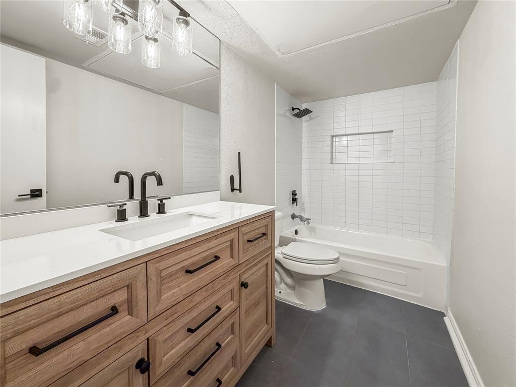 5840 Spring Valley Road, Unit 602 Dallas, TX 75254 - Photo 14 of 19 Bathroom featuring a wood-finish double vanity with a white countertop and integrated sink, matte black fixtures, a large mirror, a tiled shower-tub combination with a recessed niche, and dark gray tile flooring