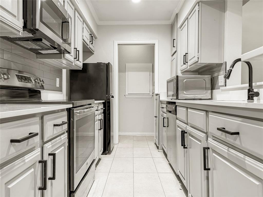 5840 Spring Valley Road, Unit 602 Dallas, TX 75254 - Photo 2 of 19 Galley kitchen featuring light-toned cabinetry with black hardware, stainless steel appliances, light countertops, a subway tile backsplash, and tile flooring